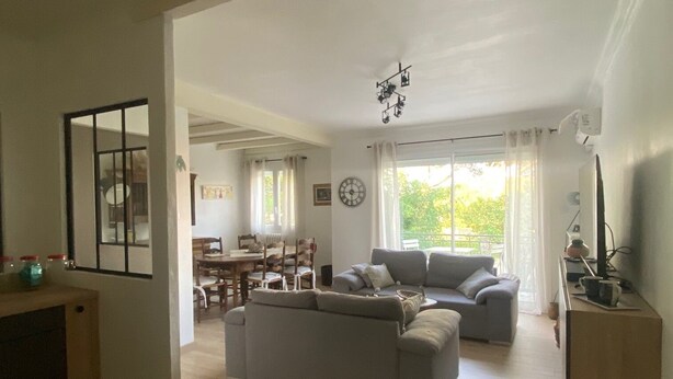 Amplia sala de estar con un sofá grande de color gris, una mesa de comedor con sillas y una cocina con mostrador y armarios.