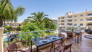 Un balcone con tavolo e sedie, vista su una piscina e vegetazione lussureggiante.