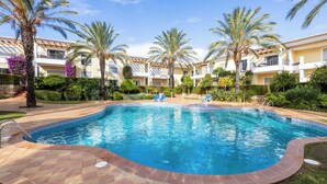 Una piscina con borda piastrellata, circondata da palme e un edificio con balconi.