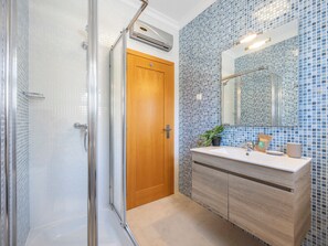 Une salle de bain avec une douche à parois de verre, une porte en bois, un lavabo avec un miroir et un mur recouvert de carreaux.