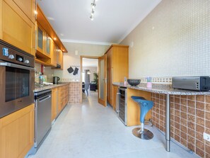 A modern kitchen with wooden cabinets, stainless steel appliances, and a blue bar stool. - Solara Ocean Retreat - apartment at Praia Porto de Mos (Lagos)