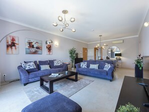 A modern living room with two sofas, a coffee table, and a dining table. There are abstract paintings on the wall, a large mirror, and a chandelier. - Solara Ocean Retreat - apartment at Praia Porto de Mos (Lagos)