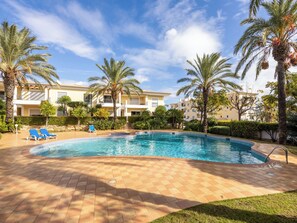 A swimming pool with a tiled deck, palm trees, and a building with balconies in the background. - Solara Ocean Retreat - apartment at Praia Porto de Mos (Lagos)