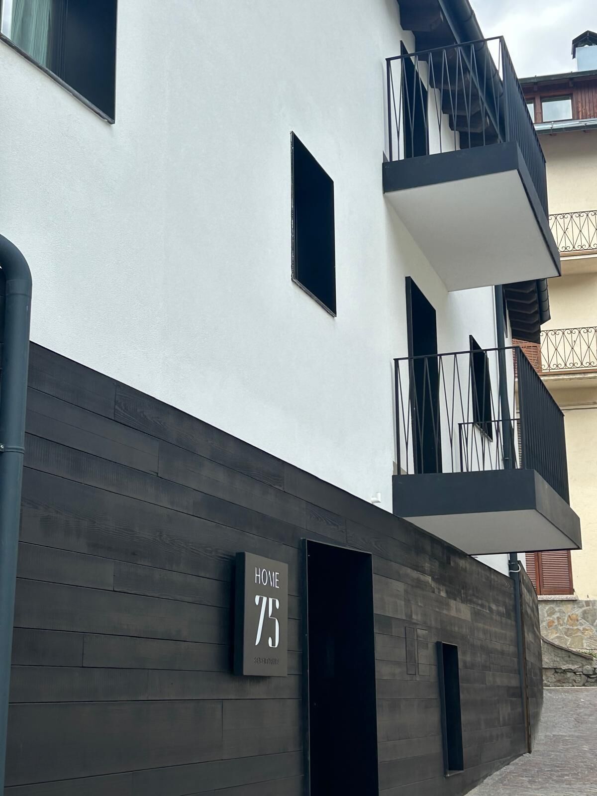 Ein modernes Gebäude mit dunkler Holzfassade, einem Balkon mit Metallgeländern und einem Schild mit der Aufschrift 'HOME 75'.