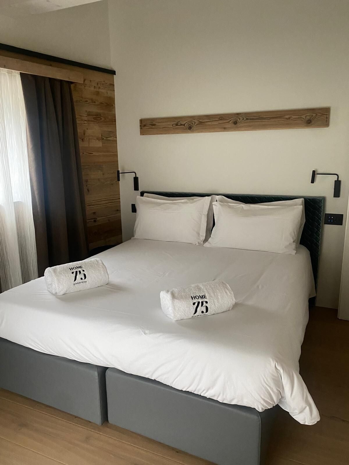 Ein Hotelzimmer mit einem Bett, einem Holz-Kopfteil, einer Wandleuchte und einem Fenster mit Vorhängen.