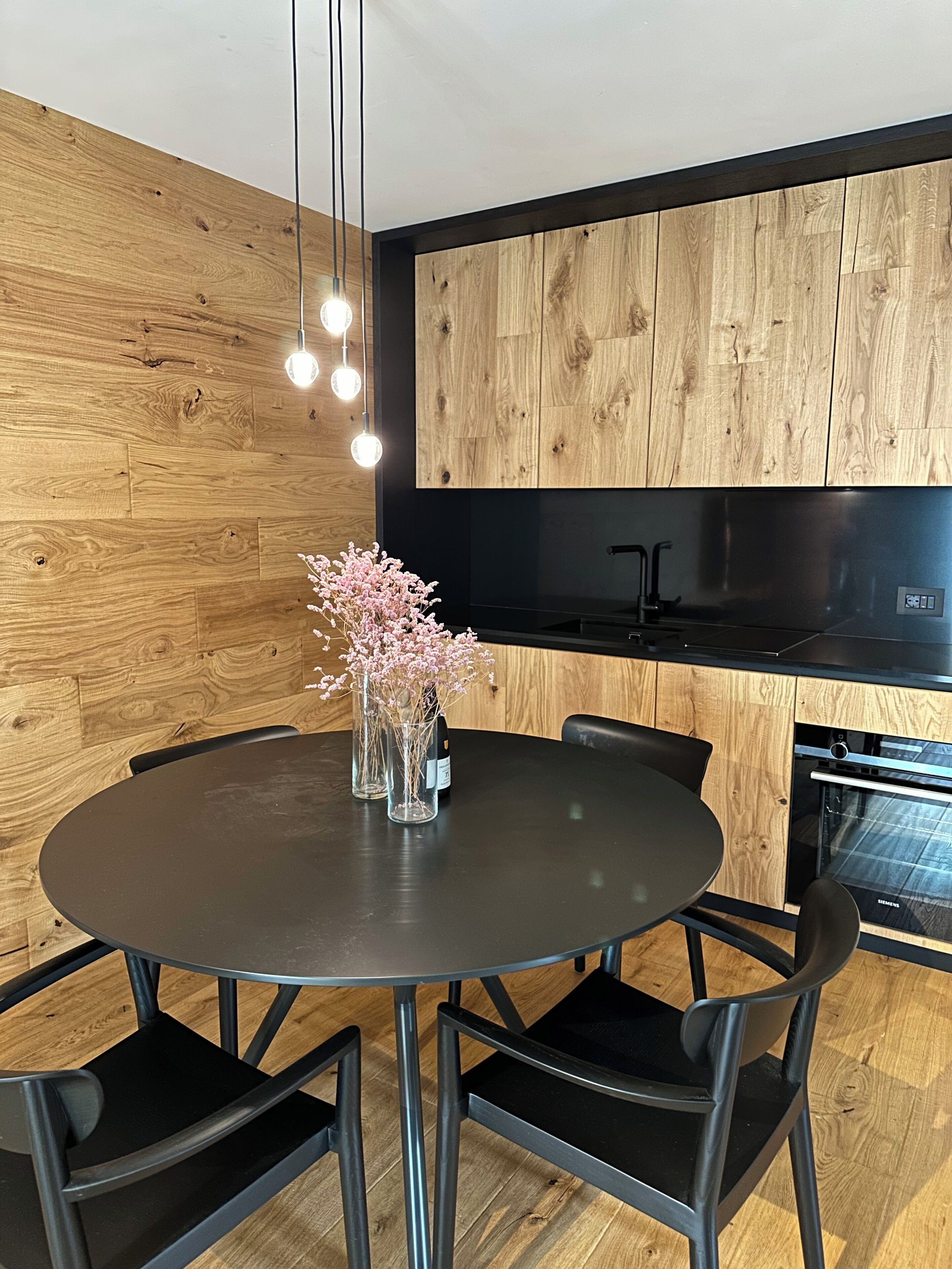 A modern kitchen with wooden paneling, a round dining table with chairs, and a built-in oven.