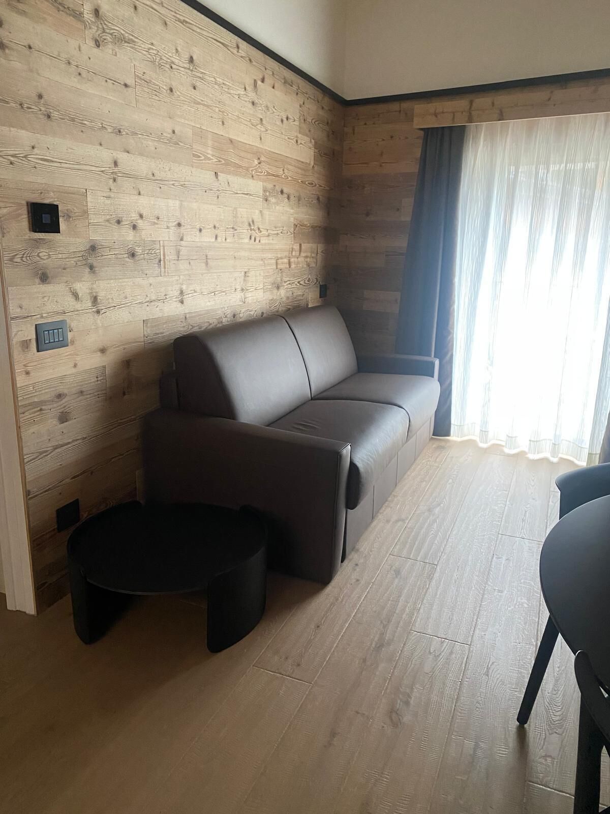 Un salon avec un mur en bois, un canapé, une table basse et une fenêtre avec des rideaux.