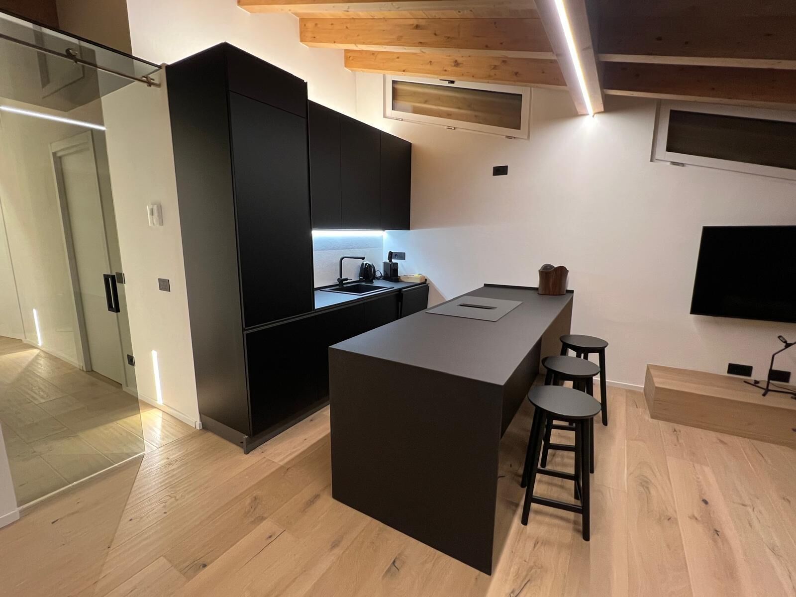Una cocina moderna con una isla central, taburetes de bar y un televisor de pantalla plana montado en la pared.