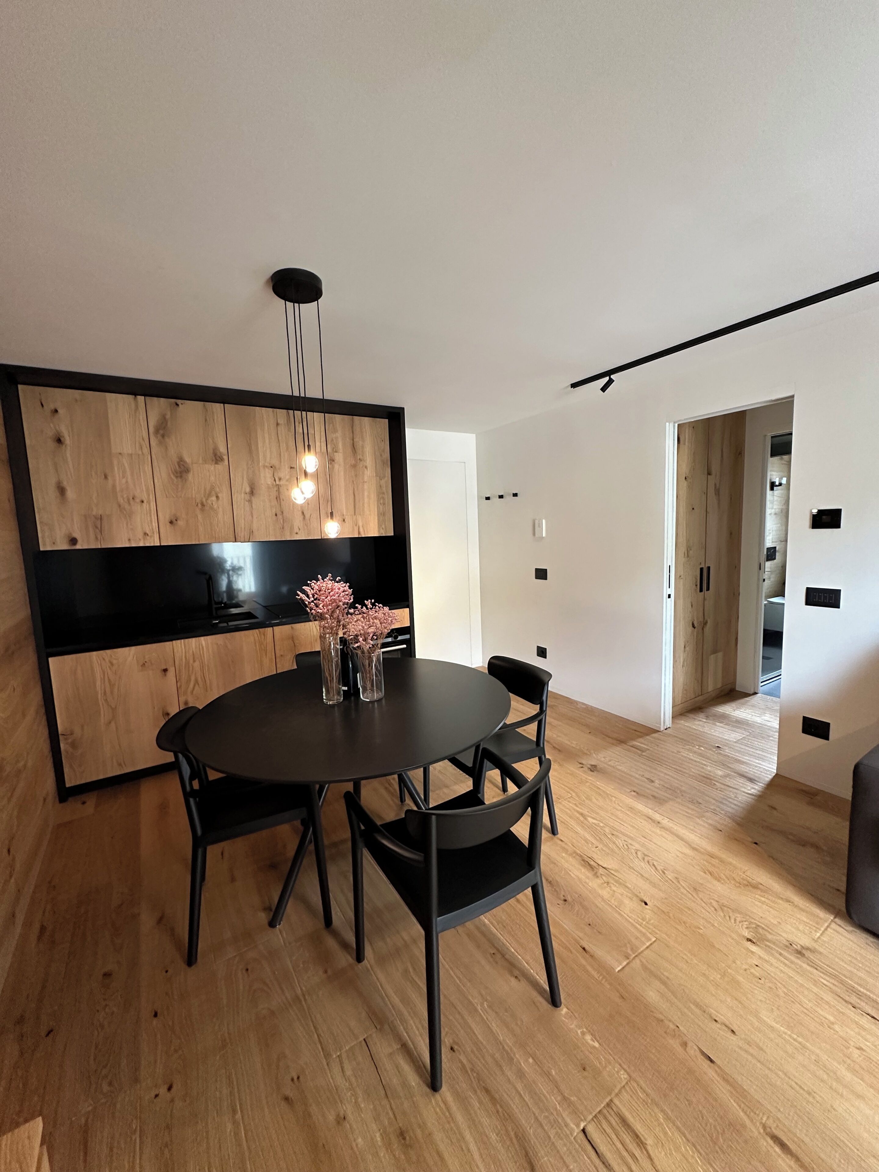 Un espace repas moderne avec une table ronde, des chaises noires, un mur d’accent en bois et un luminaire suspendu.