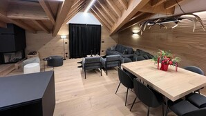 Un loft moderne avec des poutres apparentes, un coin repas doté d’une longue table et de chaises, une cheminée et un espace salon confortable avec un canapé et des fauteuils.