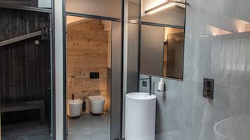 Un baño moderno con un espejo grande, un lavamanos blanco y dos inodoros.