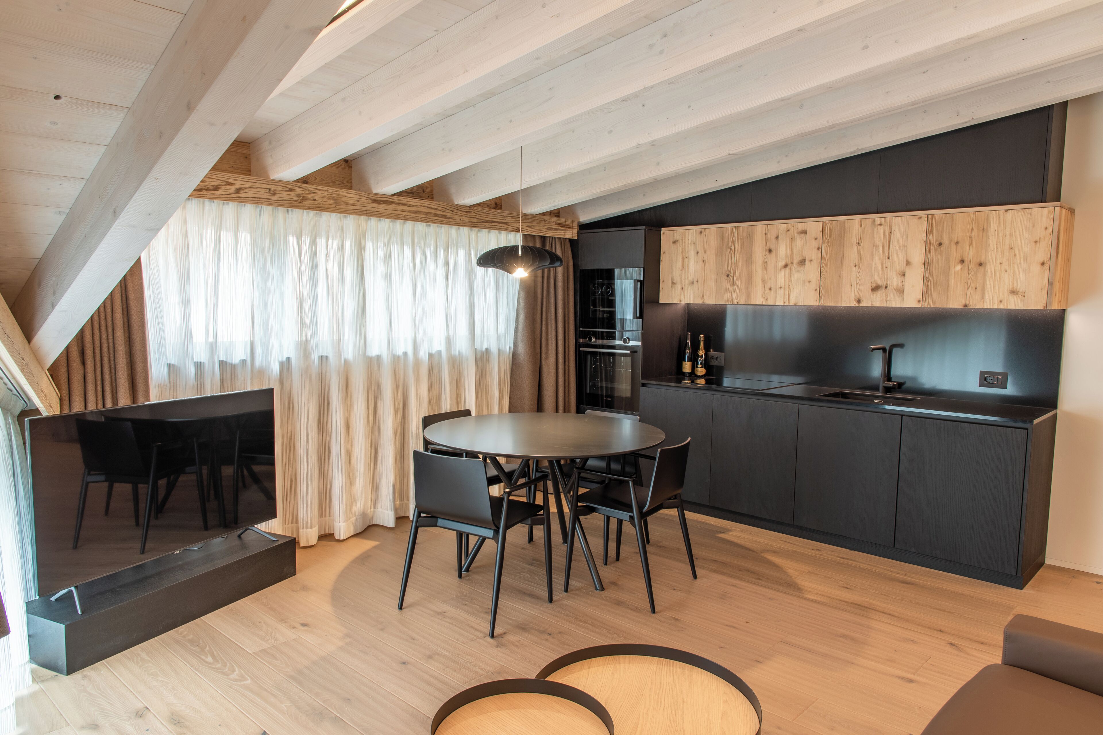 Une cuisine moderne avec des meubles de couleur sombre, un coin repas doté d’une table ronde et de chaises, et un plafond en bois.