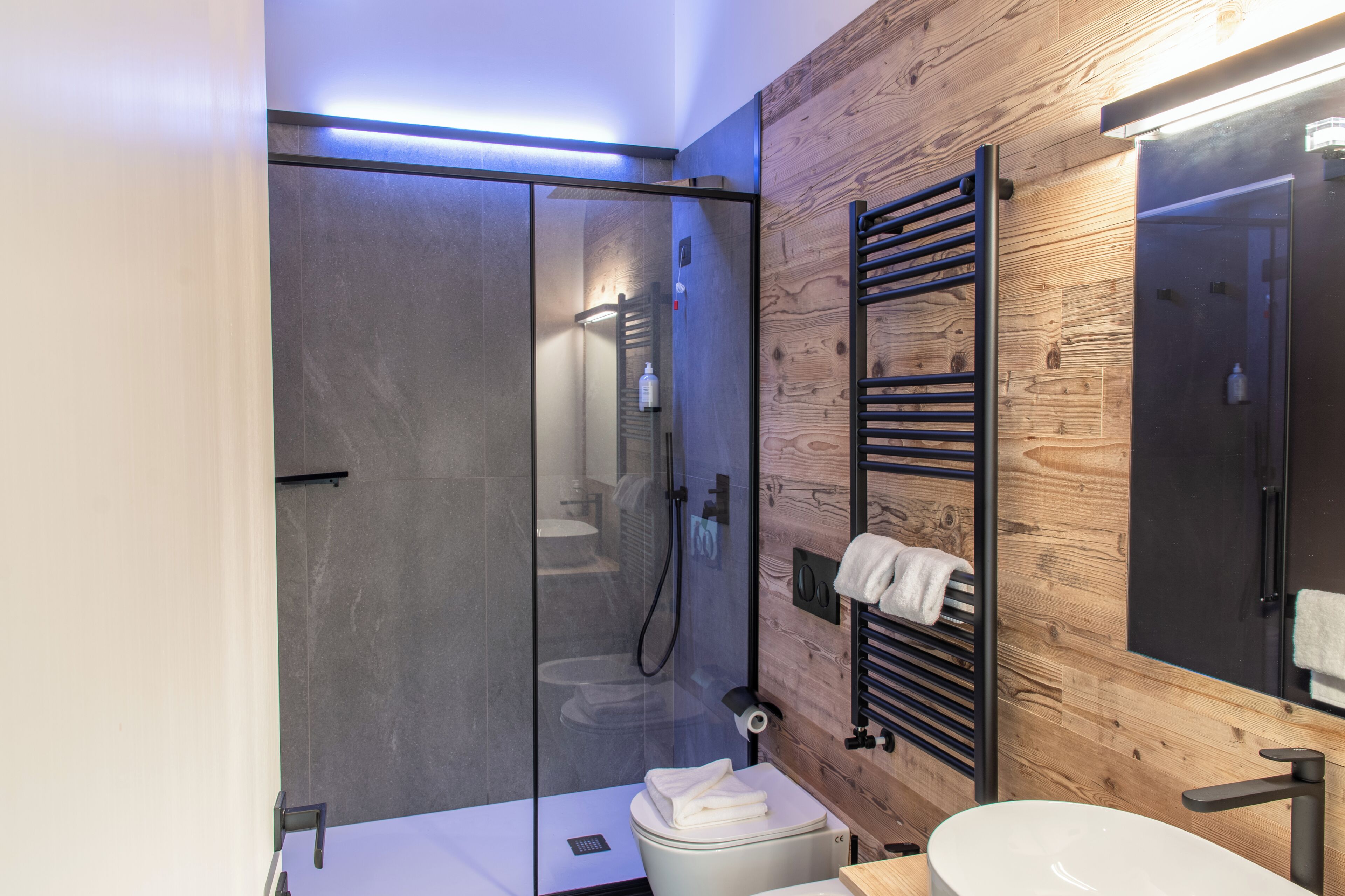 A modern bathroom with a glass-enclosed shower, a wooden wall, a towel rack, and a sink.