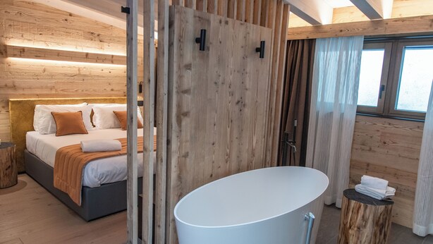 Une chambre moderne avec un grand lit, une cloison en bois, une salle de bain avec baignoire et une fenêtre avec des rideaux.
