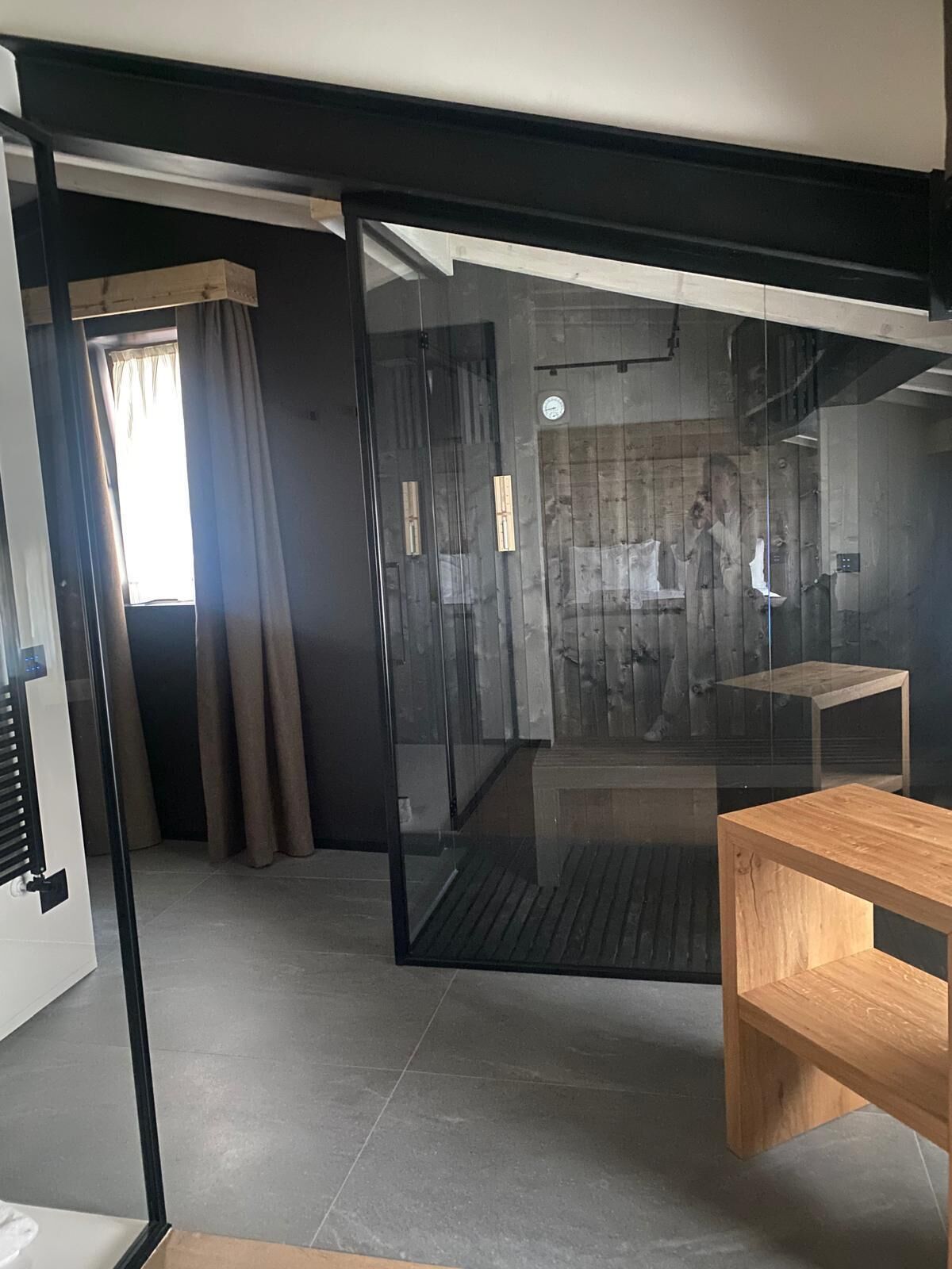 A modern room with a sliding glass door leading to a shower area, a wooden bench, and a tiled floor.