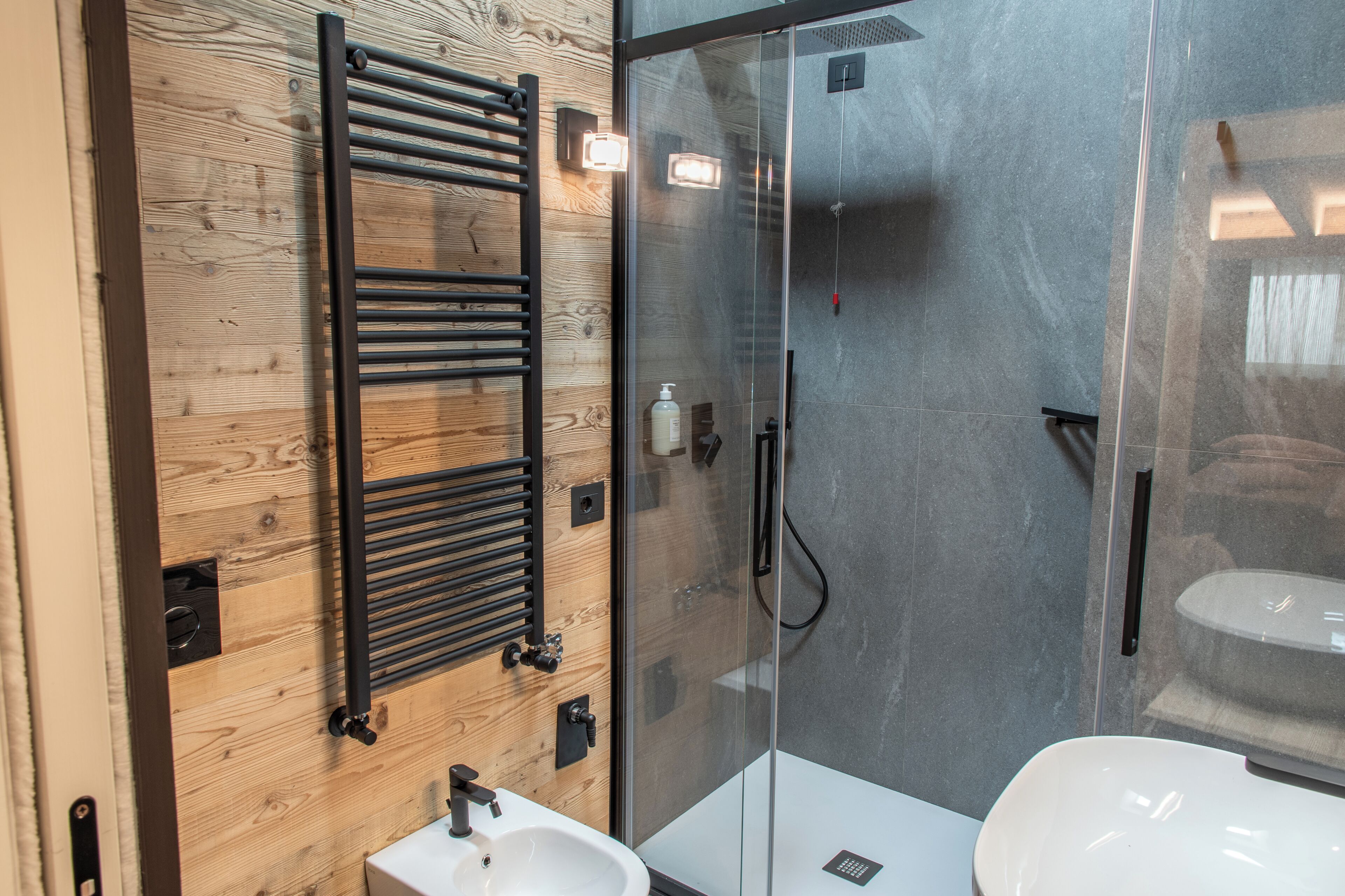 A modern bathroom with a wooden panel wall, a glass shower enclosure, and a white sink.