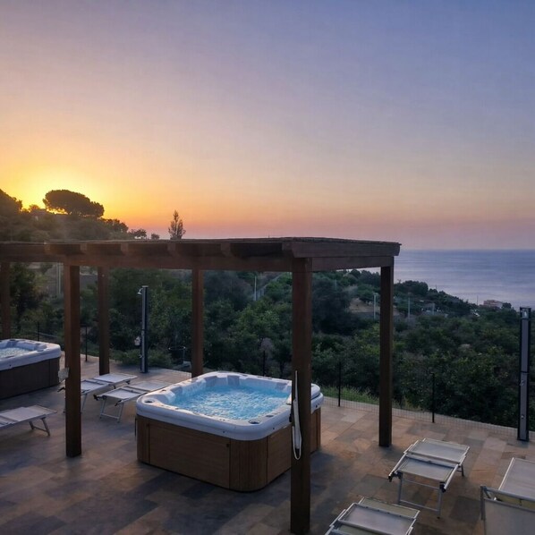 Ein Whirlpool und Liegestühle auf einer Terrasse mit Blick auf das Meer und die Hügel.