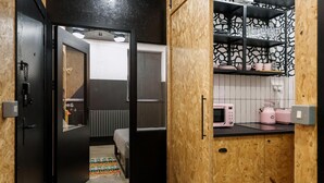 A compact kitchen with a microwave, toaster, and shelves with dishes.