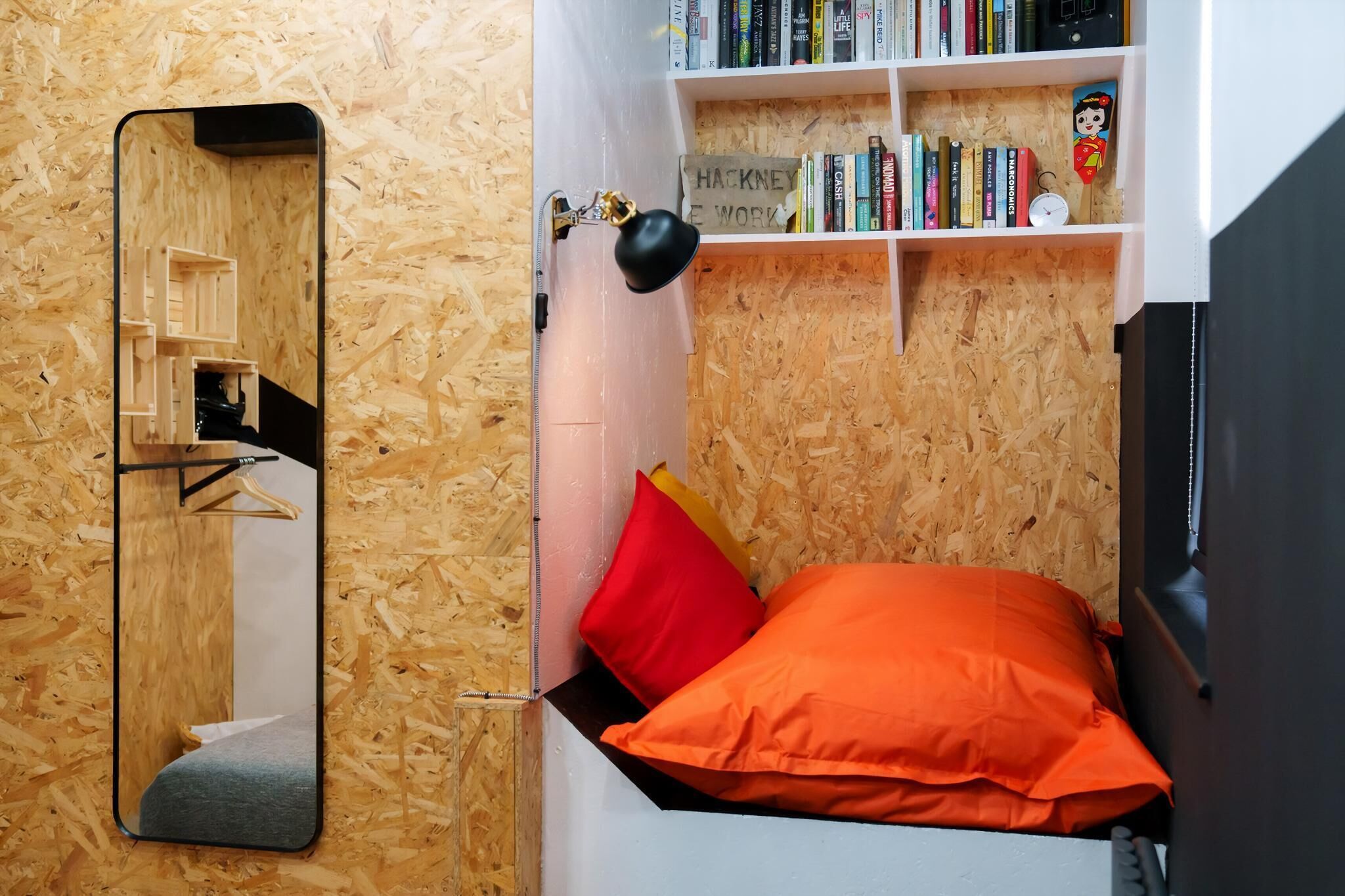 Ein gemütlicher Raum mit Holzwand, einem Bett mit orangefarbener Bettwäsche, einem Spiegel, einem Bücherregal und einer kleinen Uhr.