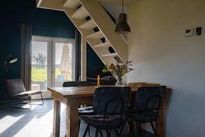En matplats med ett träbord, mörka stolar, en vas med blommor, en hängande taklampa och utsikt genom en glasdörr.