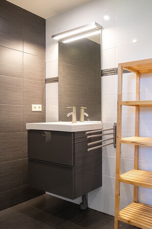 A modern bathroom with a dark-toned vanity, a large mirror, and a wooden shelf unit. - Hoeve de Binnenplaets Vrijstaand Huis (Schimmert)