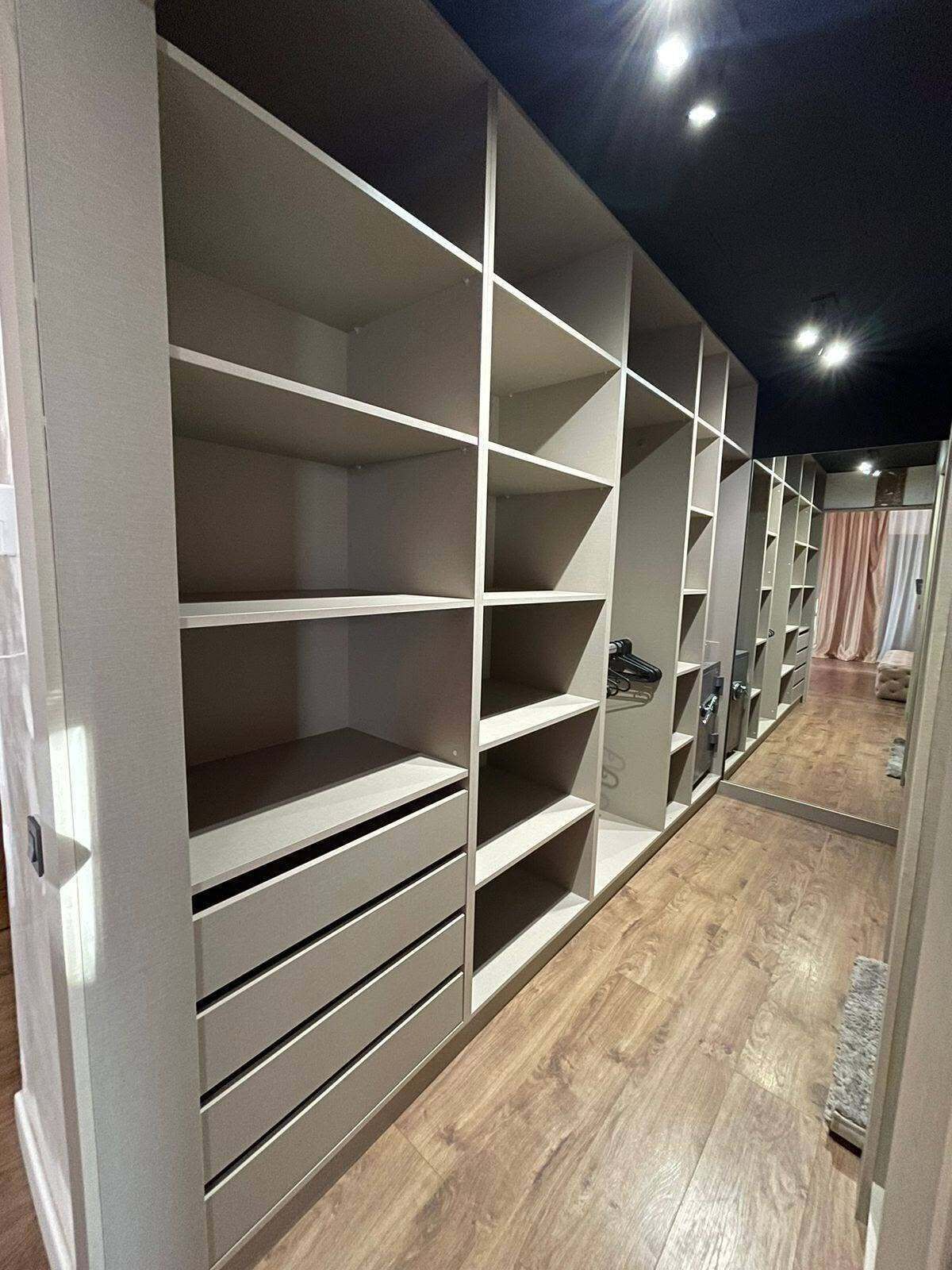 A walk-in closet with multiple shelves and drawers, wooden flooring, and a dark ceiling.