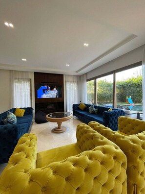Ein modernes Wohnzimmer mit großem Flachbildfernseher, zwei Sofas, einem Couchtisch und Blick auf einen Swimmingpool.