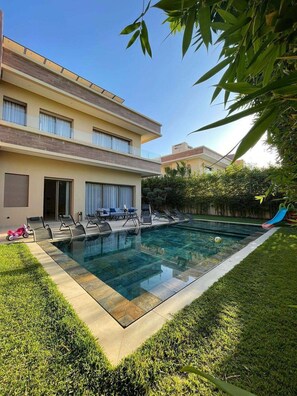 Ein modernes, zweistöckiges Haus mit Swimmingpool, Sitzgelegenheiten im Freien und einer Rutsche.