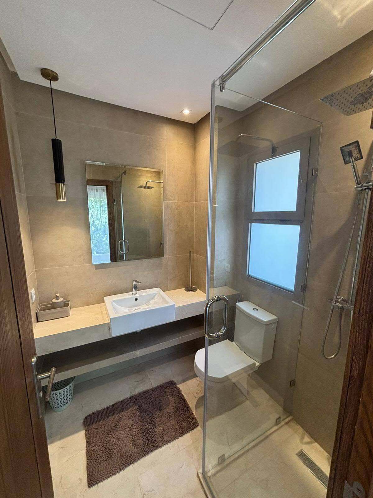 Ein modernes Badezimmer mit Duschkabine aus Glas, Waschbecken, Toilette und Spiegel.