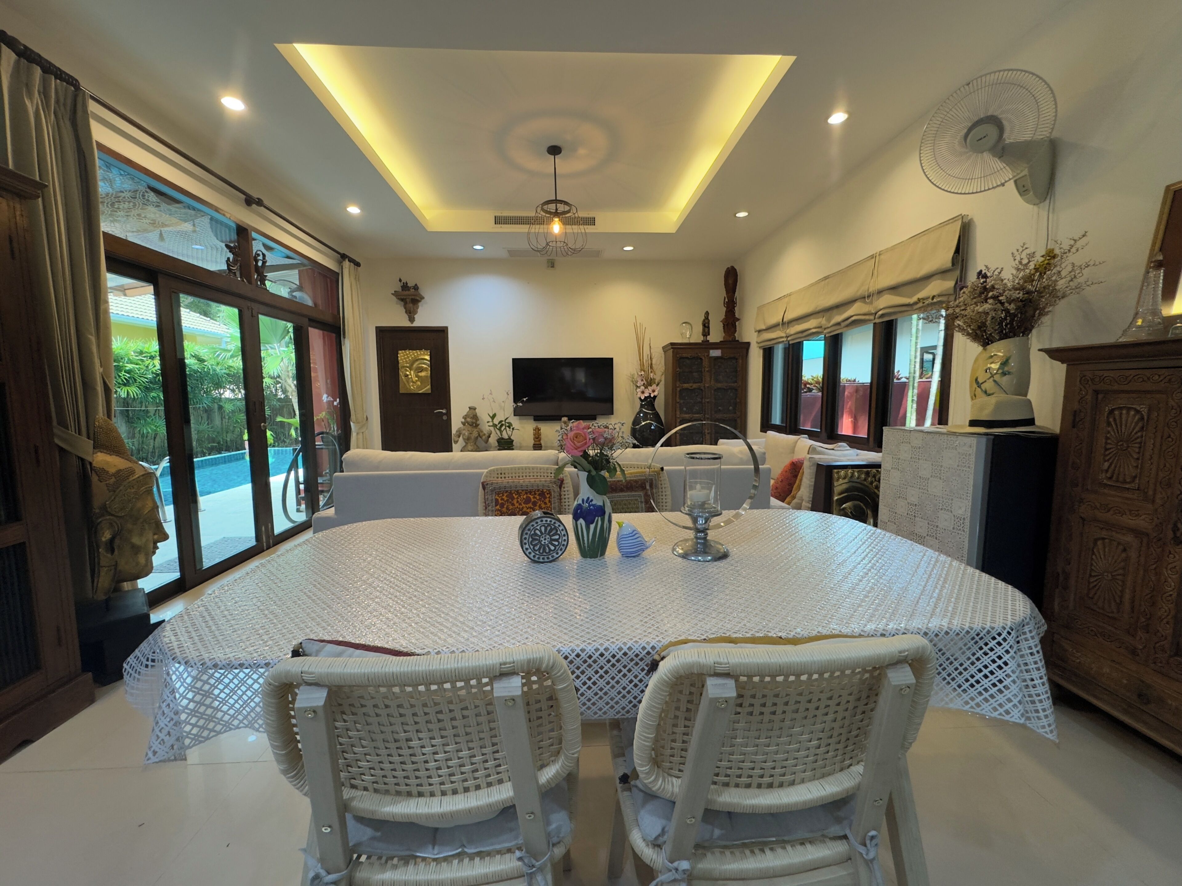 A dining area with a round table, two wicker chairs, a ceiling fan, and a TV mounted on the wall.