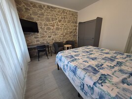 Un dormitorio con cama, un escritorio, dos sillas, un muro de piedra y un armario.