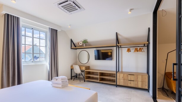 A modern hotel room with a bed, desk, TV, and storage units. - Stylish Coral Blue Condo at Bhome Punda Residences (Willemstad)