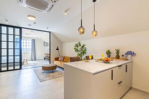 A modern kitchen with a central island, pendant lighting, and a view into the living area. - Stylish Coral Blue Condo at Bhome Punda Residences (Willemstad)