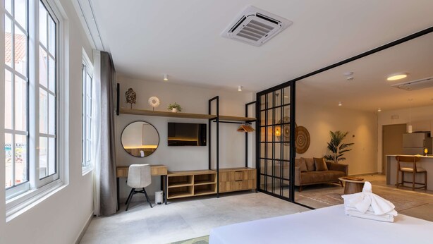 Habitación de hotel moderna con una cama grande, un escritorio, una silla, un espejo y vistas al área de la cocina.