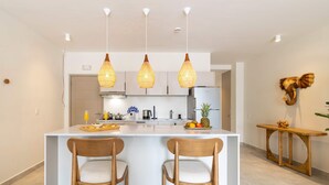 Una cocina moderna con una isla central, luces colgantes y sillas de madera.