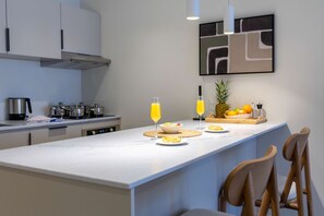 Eine moderne Küche mit Marmorarbeitsplatte, einer Kaffeemaschine, einer Obstschale und zwei Gläsern Orangensaft.