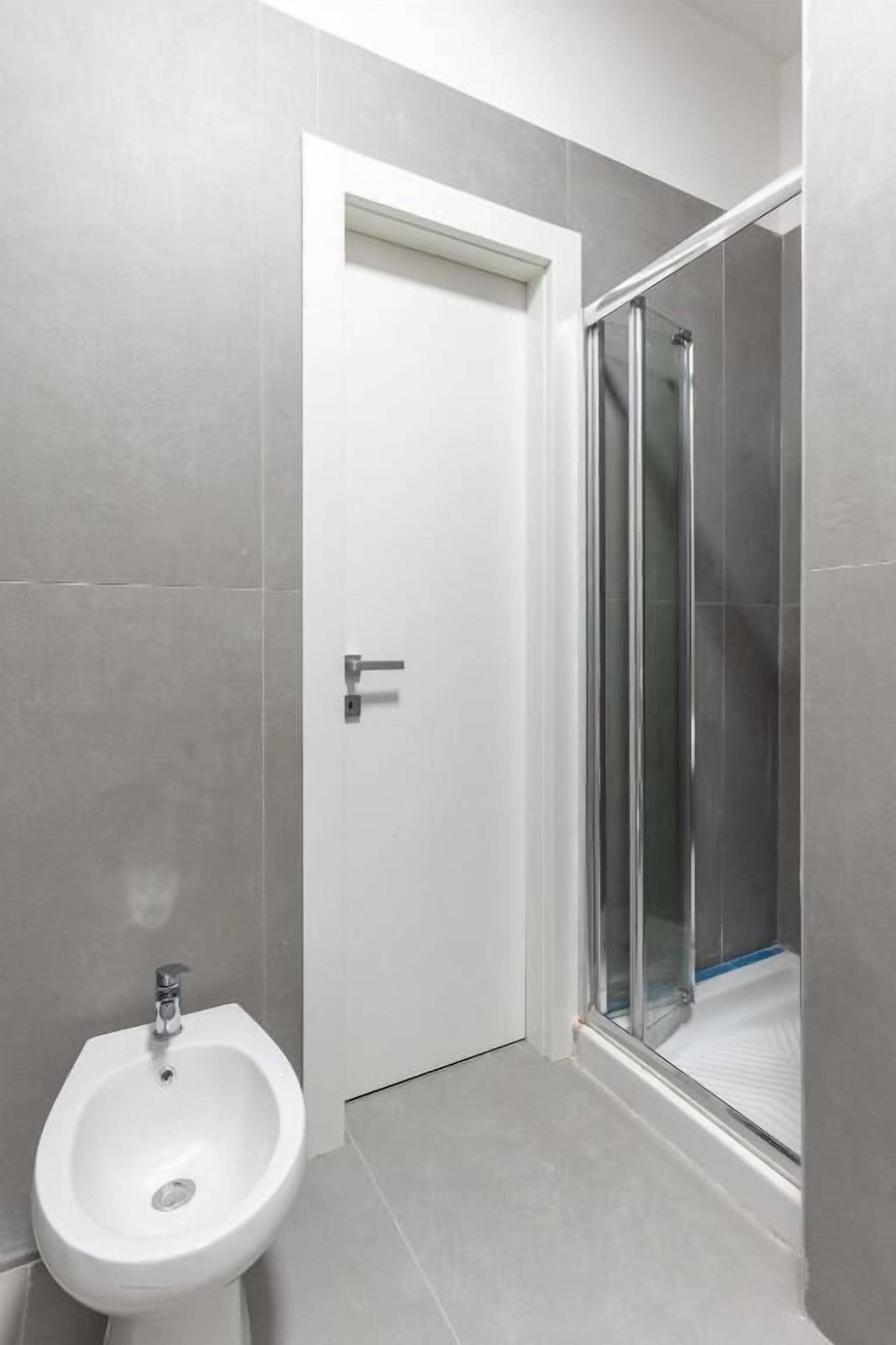Een badkamer met een bidet, een douche met glazen deuren en een witte deur.
