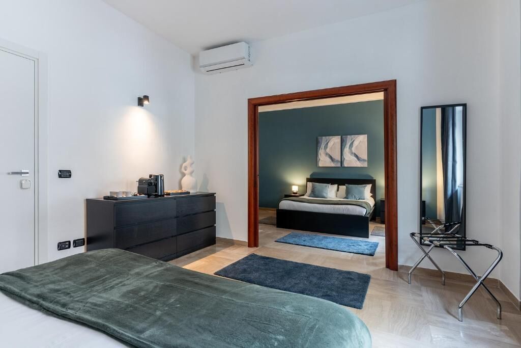 A bedroom with a bed, dresser, bedside table, lamp, and a mirror.
