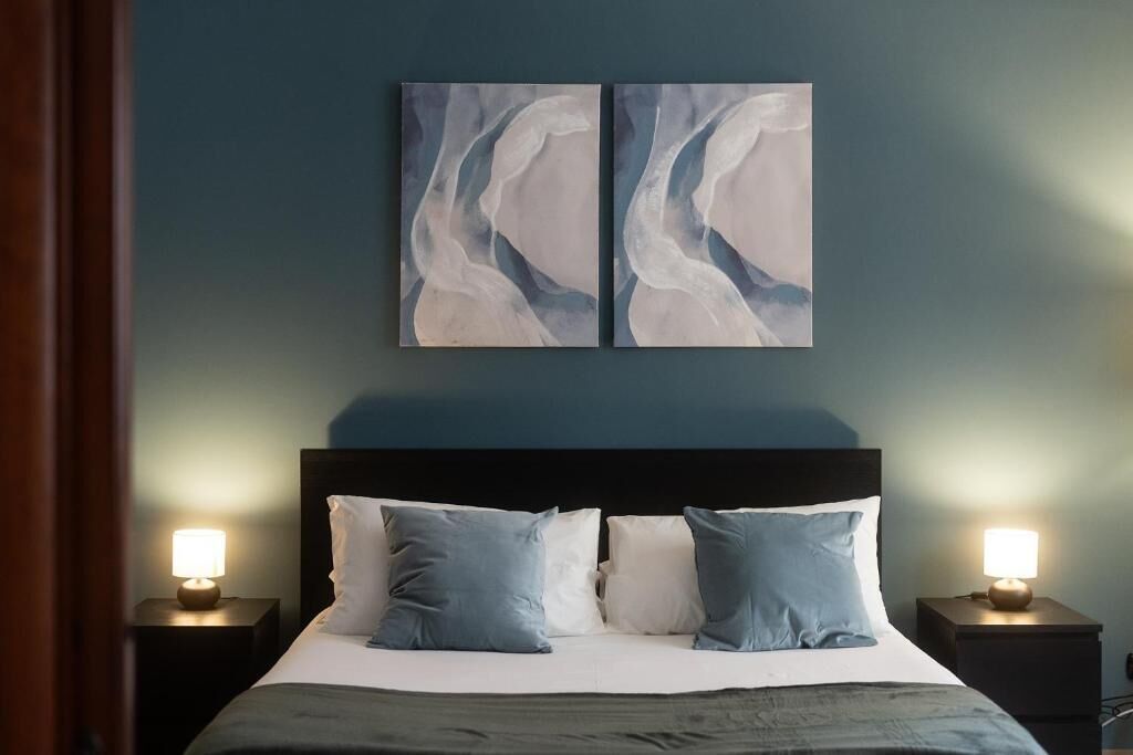 A bedroom with a bed, two bedside tables with lamps, and two abstract wall art pieces.