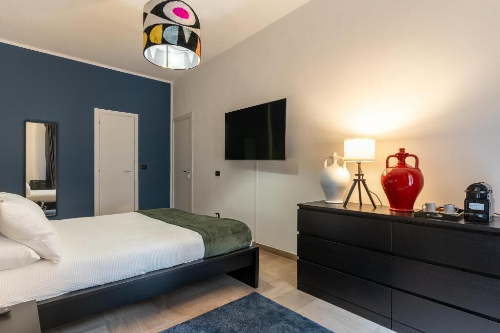 A bedroom with a bed, a dresser, a TV, and a lamp.