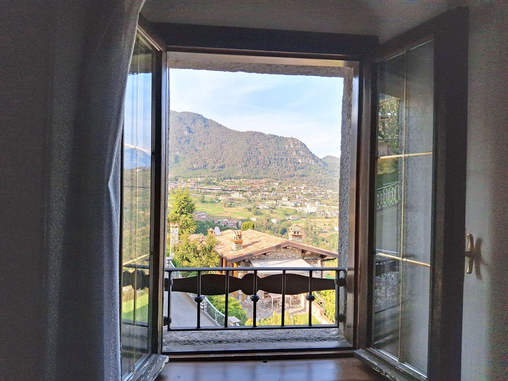 Una habitació amb un gran finestral, un balcó amb barana de metall i vista a un paisatge muntanyós.