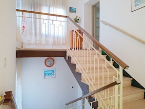 Eine Treppe mit hölzernem Geländer und weißen Spindeln, eine wandhängende Uhr und ein gerahmtes Bild.