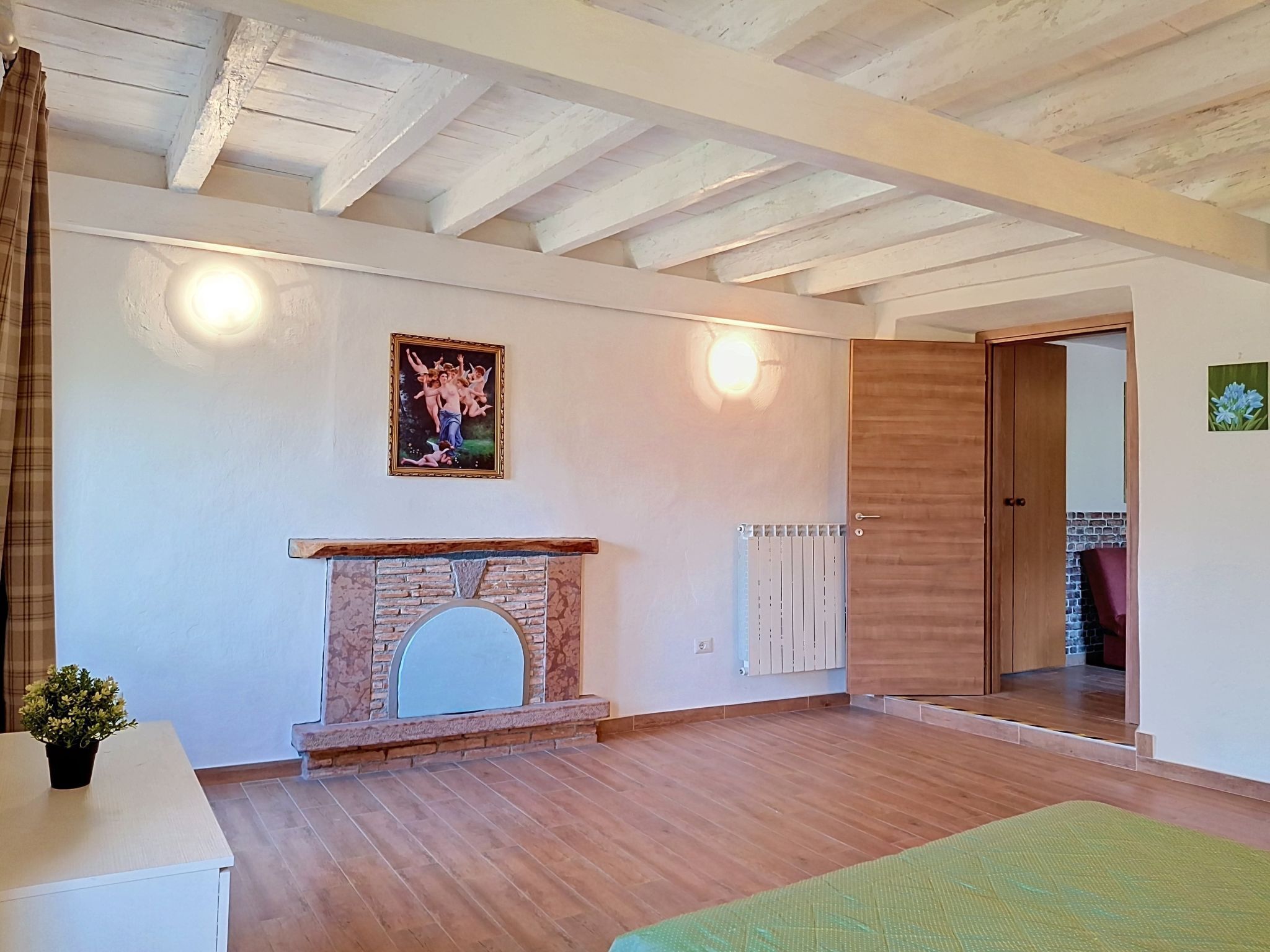 Une pièce spacieuse avec une cheminée, des poutres en bois au plafond et une porte donnant sur une autre pièce.