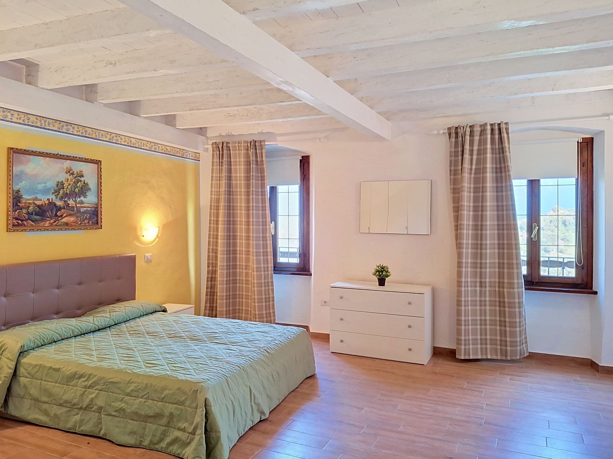 A bedroom with a bed, a dresser, a painting, and a window with curtains.