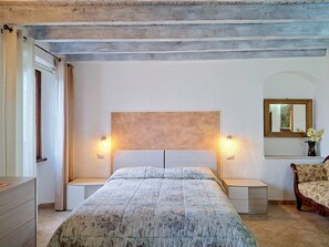 Ein Schlafzimmer mit Bett, Nachttischen, Kommode, Spiegel und einem Fenster mit Vorhängen.