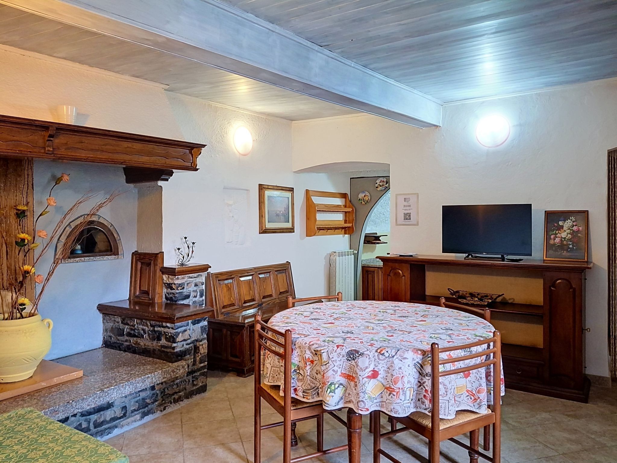 A dining area with a round table, chairs, a stone fireplace, and a television on a stand.