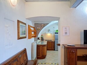 Ein schmaler Flur führt zu einer Küche mit Holzschränken, einem Heizkörper und einem gerahmten Bild an der Wand.