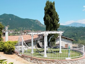 En trädgård med en pergola, en stenmur och utsikt över en stad och berg i bakgrunden.