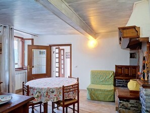 Ein Essbereich mit einem runden Tisch, Stühlen, einem grünen Sessel, einem Holzschrank und einer Heizung.