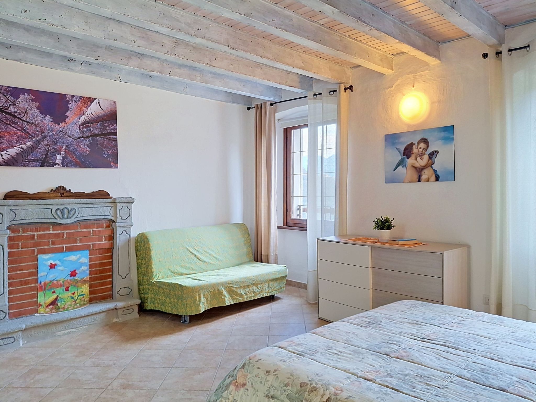 Une chambre à coucher comprenant un lit, un canapé, une commode, une cheminée et deux tableaux accrochés aux murs.